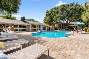 A pool surrounded by a patio with chairs and a table.